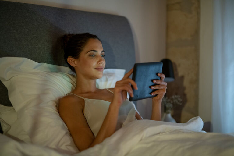 kobieta w pościeli siedzi oparta o zagłówek łóżka nocą i trzyma w ręku tablet